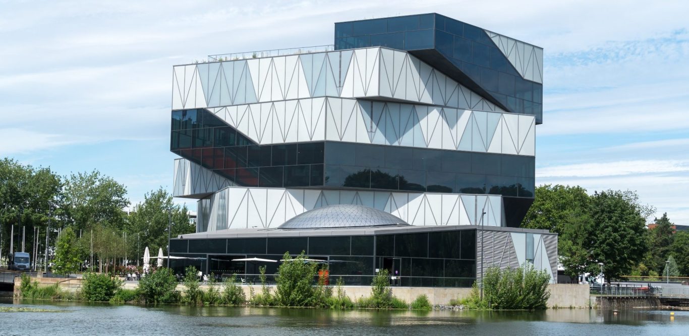 Modernes, mehrstöckiges Gebäude mit asymmetrischer Fassade und reflektierenden Glasflächen. 3D-Druckerei