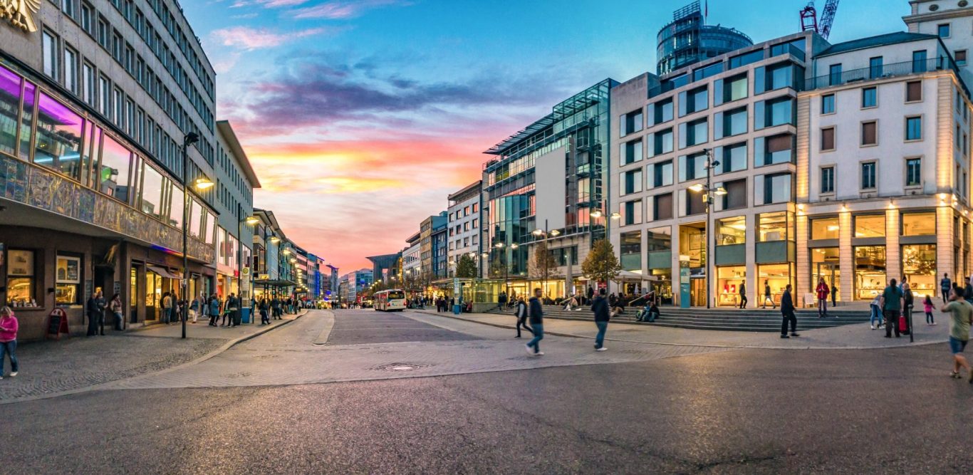 Belebte Stadtstraße bei Sonnenuntergang mit Geschäften und Passanten. 3D-Druckerei