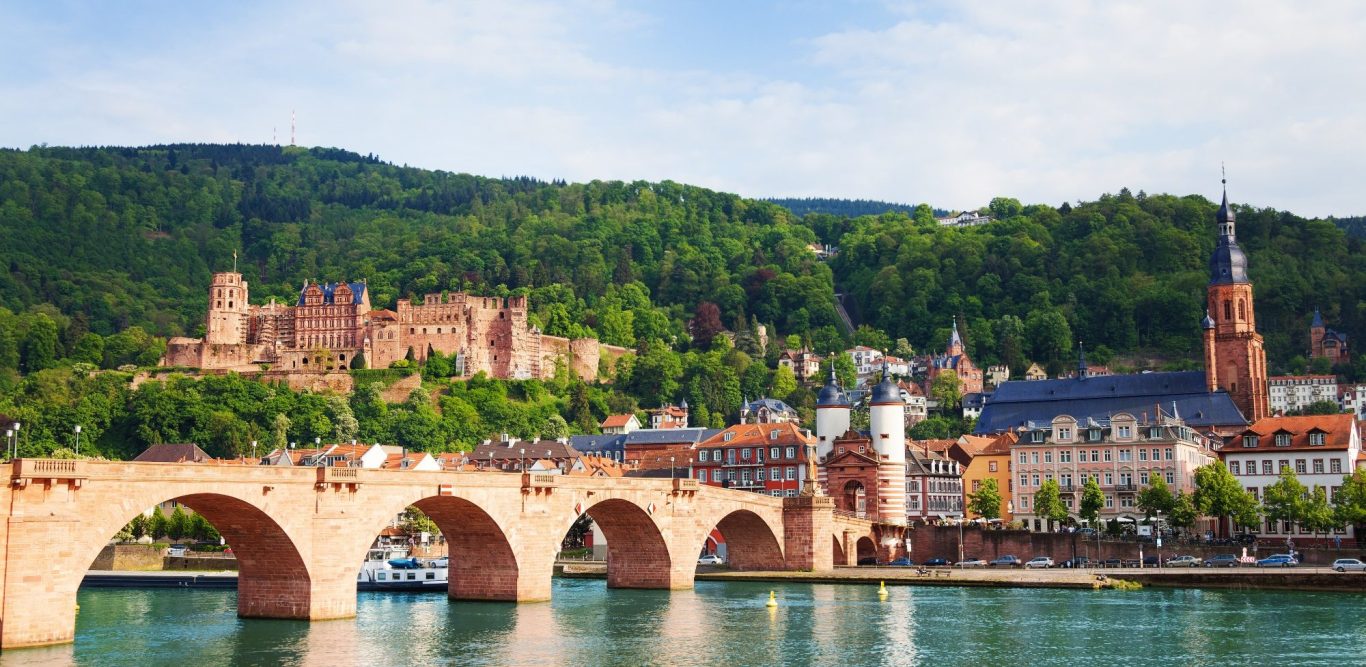 Ansicht der Heidelberger Altstadt mit Brücke, Schloss und umliegenden Hügeln.